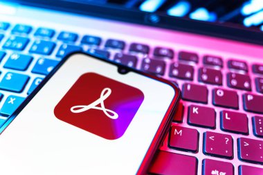 Prag, Çek Cumhuriyeti - 08 19 2025: Klavyede duran ve Akrobat Reader logosunu gösteren cep telefonunun yakından görüntüsü. Acrobat Reader, PDF belgelerini görüntülemek ve yönetmek için bir platformdur.