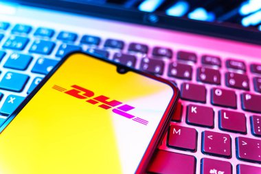 Prag, Çek Cumhuriyeti - 08 19 2025: DHL logosunu gösteren klavyenin üzerinde duran cep telefonunun yakından görüntüsü. DHL uluslararası nakliye hizmeti sunan bir lojistik şirketidir..