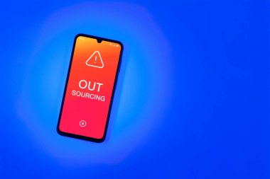 Arka plandaki telefon dış kaynak metnini gösteriyor. Dış kaynak kullanımı belli görevler için dış sağlayıcıları işe almaktır.