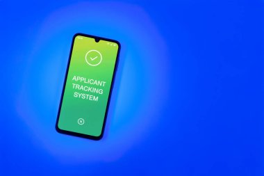 Sade arkaplandaki telefon Uygulamalı İzleme Sistemi metnini gösteriyor. Başvuru İzleme Sistemi işe alım süreçlerini yönetmek için bir yazılımdır.