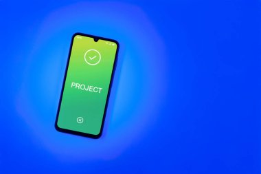 Sade arkaplandaki telefon Proje metnini gösteriyor. Proje, tanımlanmış hedefleri ve son teslim tarihleriyle planlandı.