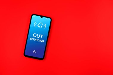 Arka plandaki telefon dış kaynak metnini gösteriyor. Dış kaynak kullanımı belli görevler için dış sağlayıcıları işe almaktır.