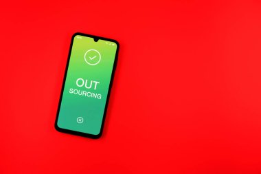 Arka plandaki telefon dış kaynak metnini gösteriyor. Dış kaynak kullanımı belli görevler için dış sağlayıcıları işe almaktır.