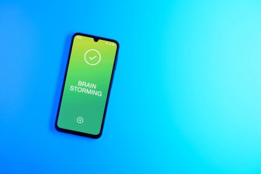 Arka plandaki telefon Beyin Fırtınası metnini gösteriyor. Beyin fırtınası grup tartışması yoluyla fikirler üretmektir..