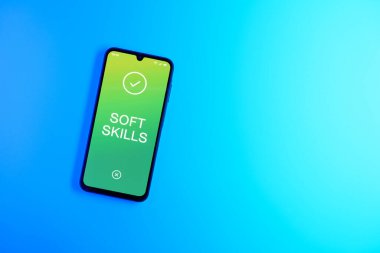 Sade arkaplandaki telefon, Soft skills metnini gösteriyor. Yumuşak beceriler, insanlar arası iletişim yetenekleridir..