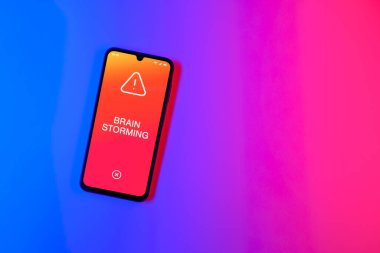 Arka plandaki telefon Beyin Fırtınası metnini gösteriyor. Beyin fırtınası grup tartışması yoluyla fikirler üretmektir..