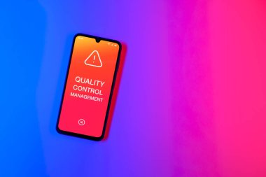 Sade arka plandaki telefon Kalite Kontrol Yönetimi metnini gösteriyor. Kalite Kontrol Yönetimi ürün veya hizmetlerin standartları karşılamasını sağlıyor.