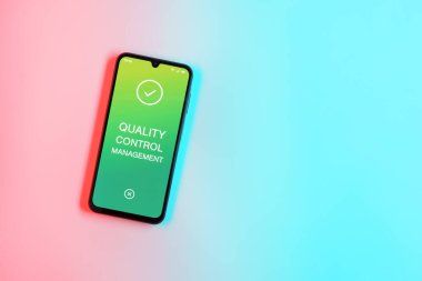 Sade arka plandaki telefon Kalite Kontrol Yönetimi metnini gösteriyor. Kalite Kontrol Yönetimi ürün veya hizmetlerin standartları karşılamasını sağlıyor.