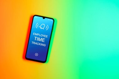 Sade arka plandaki telefon, Çalışan Zaman İzleme metnini gösteriyor. Çalışan Zaman İzleme, çalışanların çalışma saatlerini kaydediyor..