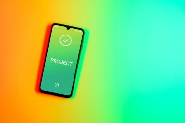 Sade arkaplandaki telefon Proje metnini gösteriyor. Proje, tanımlanmış hedefleri ve son teslim tarihleriyle planlandı.