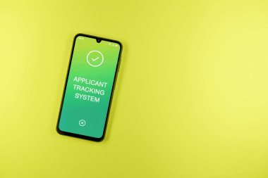 Sade arkaplandaki telefon Uygulamalı İzleme Sistemi metnini gösteriyor. Başvuru İzleme Sistemi işe alım süreçlerini yönetmek için bir yazılımdır.
