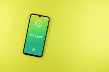 Sade arkaplandaki telefon Proje metnini gösteriyor. Proje, tanımlanmış hedefleri ve son teslim tarihleriyle planlandı.