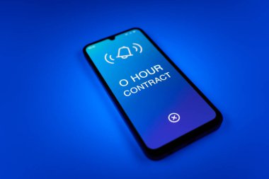 Üniformalı bir arkaplanda duran cep telefonunun ayrıntıları. O Saat Sözleşmesi metni. O Saat Sözleşmesi garantili çalışma saatleri olmayan bir sözleşmedir..