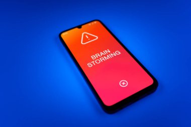 Tek bir arka planda duran cep telefonunun ayrıntıları Beyin Fırtınası metnini gösteriyor. Beyin fırtınası grup tartışması yoluyla fikirler üretmektir..