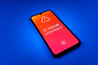 Üniformalı bir arkaplanda duran cep telefonunun ayrıntıları. O Saat Sözleşmesi metni. O Saat Sözleşmesi garantili çalışma saatleri olmayan bir sözleşmedir..