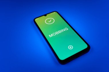 Üniformalı bir arka planda duran cep telefonunun Mobbing metnini gösteren bir detayı. Gangsterlik iş arkadaşları arasında zorbalıktır..