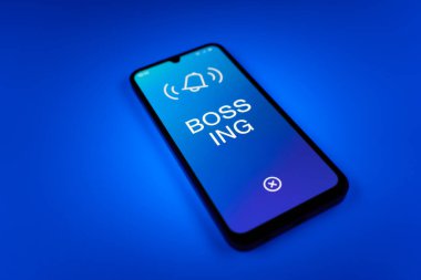 Üniformalı bir arka planda duran cep telefonunun ayrıntıları Bossing 'in mesajlarını gösteriyor. Patronluk, amirin zorbalık ettiği işyeridir..