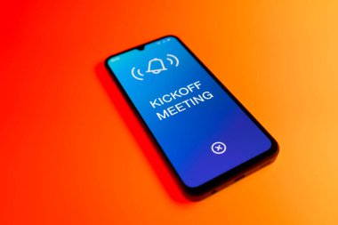 Üniformalı bir arka planda duran cep telefonunun başlangıç mesajlarını gösteren bir detayı. Başlangıç Toplantısı bir projeye başlanacak ilk toplantı.