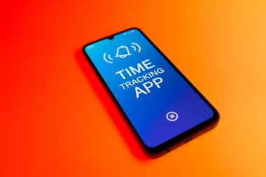 Üniformalı bir arka planda bulunan ve mesaj Zaman İzleme Uygulamasını gösteren bir cep telefonunun ayrıntısı. Zaman İzleme Uygulaması günlük kaydı çalışma saatleri için bir yazılımdır.