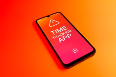 Üniformalı bir arka planda bulunan ve mesaj Zaman İzleme Uygulamasını gösteren bir cep telefonunun ayrıntısı. Zaman İzleme Uygulaması günlük kaydı çalışma saatleri için bir yazılımdır.