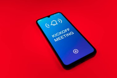 Üniformalı bir arka planda duran cep telefonunun başlangıç mesajlarını gösteren bir detayı. Başlangıç Toplantısı bir projeye başlanacak ilk toplantı.