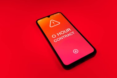 Üniformalı bir arkaplanda duran cep telefonunun ayrıntıları. O Saat Sözleşmesi metni. O Saat Sözleşmesi garantili çalışma saatleri olmayan bir sözleşmedir..