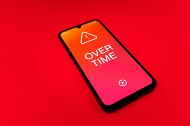 Üniformalı bir arkaplanda yatan cep telefonunun fazla mesai mesajlarını gösteren bir detayı. Fazla mesai normal çalışma saatlerinin ötesinde yapılır..