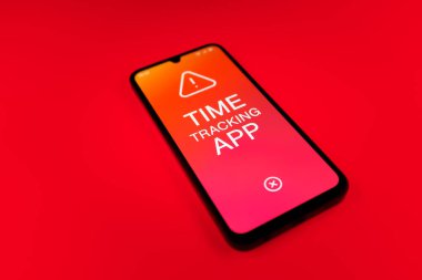 Üniformalı bir arka planda bulunan ve mesaj Zaman İzleme Uygulamasını gösteren bir cep telefonunun ayrıntısı. Zaman İzleme Uygulaması günlük kaydı çalışma saatleri için bir yazılımdır.