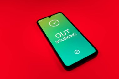 Üniformalı bir arka planda duran cep telefonunun dış kaynak metnini gösteren bir detayı. Dış kaynak kullanımı belli görevler için dış sağlayıcıları işe almaktır.