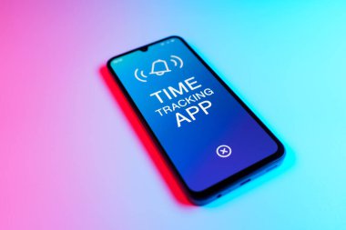 Üniformalı bir arka planda bulunan ve mesaj Zaman İzleme Uygulamasını gösteren bir cep telefonunun ayrıntısı. Zaman İzleme Uygulaması günlük kaydı çalışma saatleri için bir yazılımdır.