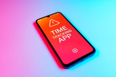 Üniformalı bir arka planda bulunan ve mesaj Zaman İzleme Uygulamasını gösteren bir cep telefonunun ayrıntısı. Zaman İzleme Uygulaması günlük kaydı çalışma saatleri için bir yazılımdır.
