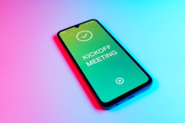 Üniformalı bir arka planda duran cep telefonunun başlangıç mesajlarını gösteren bir detayı. Başlangıç Toplantısı bir projeye başlanacak ilk toplantı.