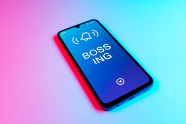 Üniformalı bir arka planda duran cep telefonunun ayrıntıları Bossing 'in mesajlarını gösteriyor. Patronluk, amirin zorbalık ettiği işyeridir..