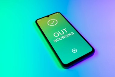 Üniformalı bir arka planda duran cep telefonunun dış kaynak metnini gösteren bir detayı. Dış kaynak kullanımı belli görevler için dış sağlayıcıları işe almaktır.