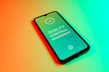 Metin Kalite Kontrol Yönetimi 'ni gösteren bir cep telefonu detayı. Kalite Kontrol Yönetimi ürün veya hizmetlerin standartları karşılamasını sağlıyor.