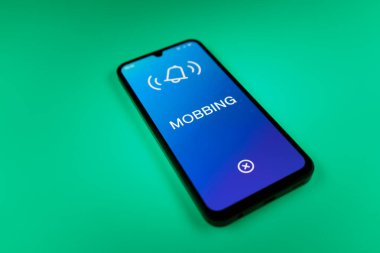 Üniformalı bir arka planda duran cep telefonunun Mobbing metnini gösteren bir detayı. Gangsterlik iş arkadaşları arasında zorbalıktır..