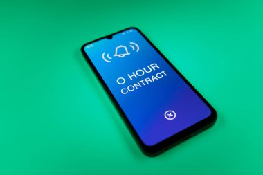 Üniformalı bir arkaplanda duran cep telefonunun ayrıntıları. O Saat Sözleşmesi metni. O Saat Sözleşmesi garantili çalışma saatleri olmayan bir sözleşmedir..