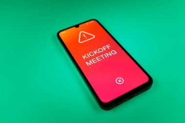 Üniformalı bir arka planda duran cep telefonunun başlangıç mesajlarını gösteren bir detayı. Başlangıç Toplantısı bir projeye başlanacak ilk toplantı.