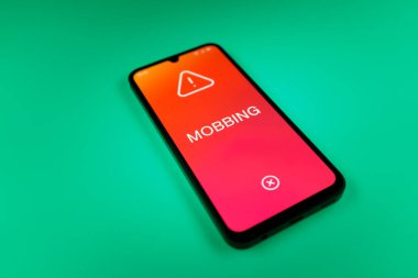 Üniformalı bir arka planda duran cep telefonunun Mobbing metnini gösteren bir detayı. Gangsterlik iş arkadaşları arasında zorbalıktır..