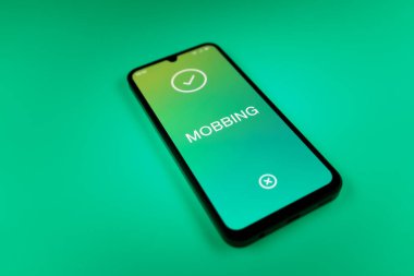 Üniformalı bir arka planda duran cep telefonunun Mobbing metnini gösteren bir detayı. Gangsterlik iş arkadaşları arasında zorbalıktır..