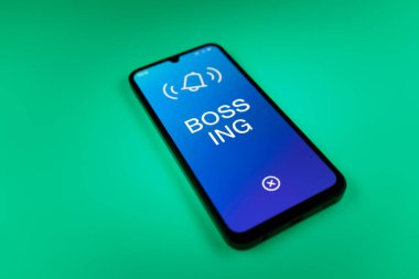 Üniformalı bir arka planda duran cep telefonunun ayrıntıları Bossing 'in mesajlarını gösteriyor. Patronluk, amirin zorbalık ettiği işyeridir..