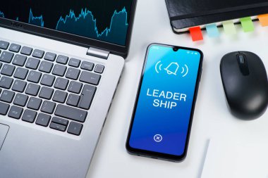 Ofis masası dizüstü bilgisayarlı ve telefonlu Liderlik metnini gösteriyor. Liderlik bir takıma rehberlik etme ve onlara ilham verme yeteneğidir..