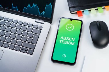 Ofis masası dizüstü bilgisayar ve telefonuyla devamsızlık metnini gösteriyor. Geçerli nedenler olmadan devamsızlık sık sık işten yoksunluktur.