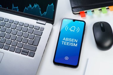 Ofis masası dizüstü bilgisayar ve telefonuyla devamsızlık metnini gösteriyor. Geçerli nedenler olmadan devamsızlık sık sık işten yoksunluktur.