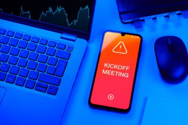 Office desk setup with laptop and phone showing Kickoff Meeting text. Kickoff Meeting is the first meeting to start a project.