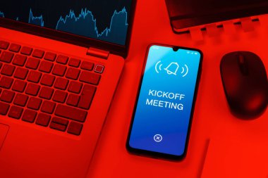 Office desk setup with laptop and phone showing Kickoff Meeting text. Kickoff Meeting is the first meeting to start a project.