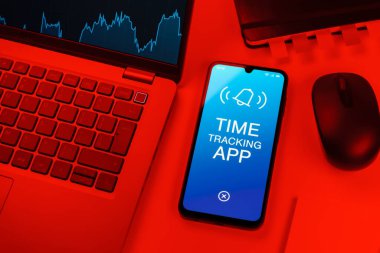Office desk setup with laptop and phone showing Time Tracking App text. Time Tracking App is software for logging work hours.