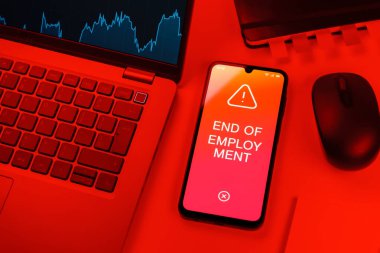 Office desk setup with laptop and phone showing End of Employment text. End of Employment is termination of the working relationship.