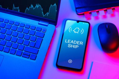 Ofis masası dizüstü bilgisayarlı ve telefonlu Liderlik metnini gösteriyor. Liderlik bir takıma rehberlik etme ve onlara ilham verme yeteneğidir..