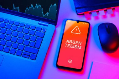 Ofis masası dizüstü bilgisayar ve telefonuyla devamsızlık metnini gösteriyor. Geçerli nedenler olmadan devamsızlık sık sık işten yoksunluktur.